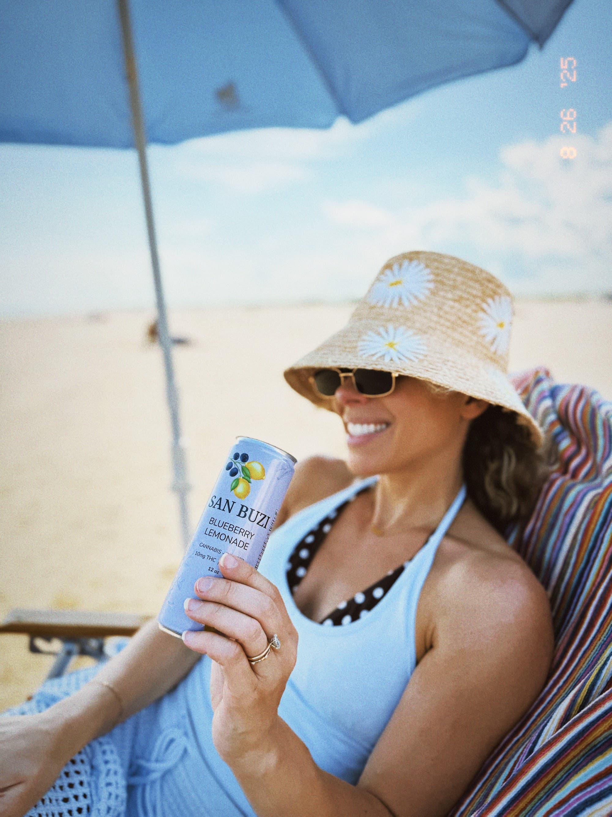 Woman relaxing on a beach lounge chair holding a can of San Buzi Blueberry Lemonade